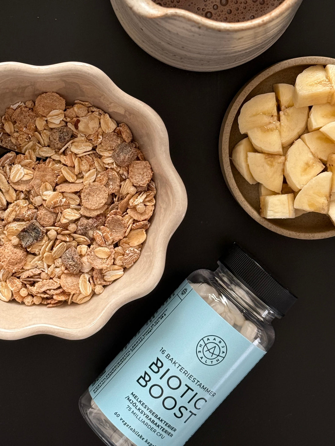 Biotic Boost probiotika med 16 bakteriestammer ved siden av frokostskål med müsli, banan og kakao